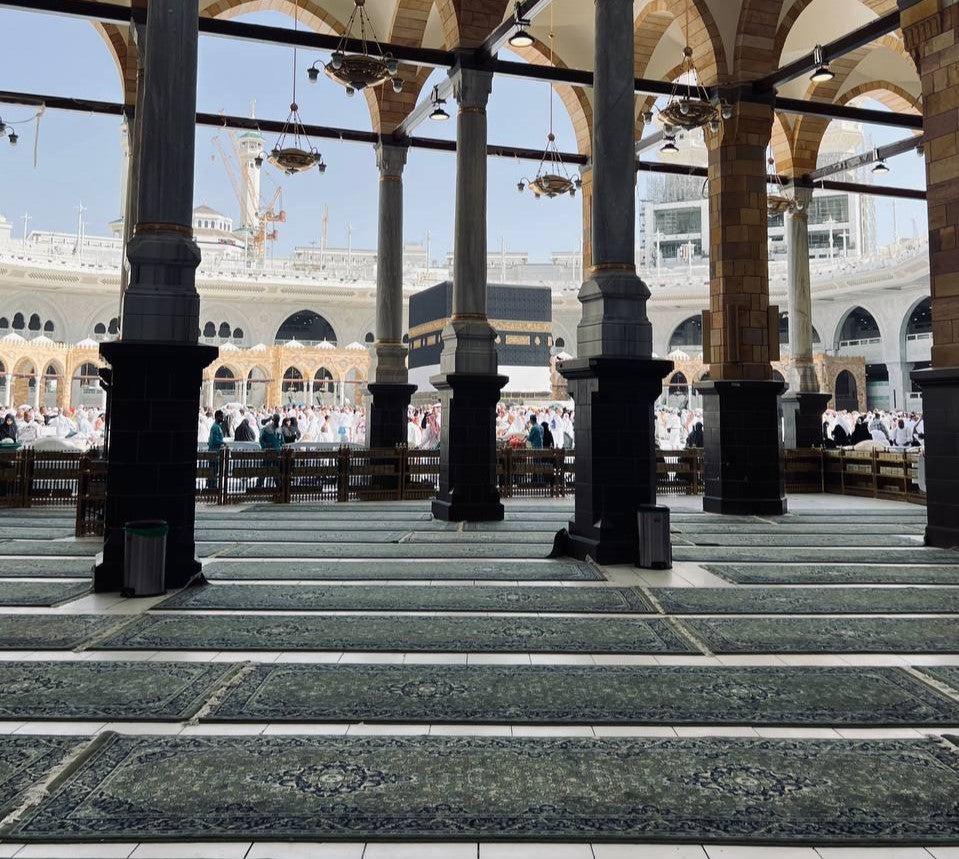 A panoramic view of the green carpets in the Masjid al-Haram, with view of the Kaabah.